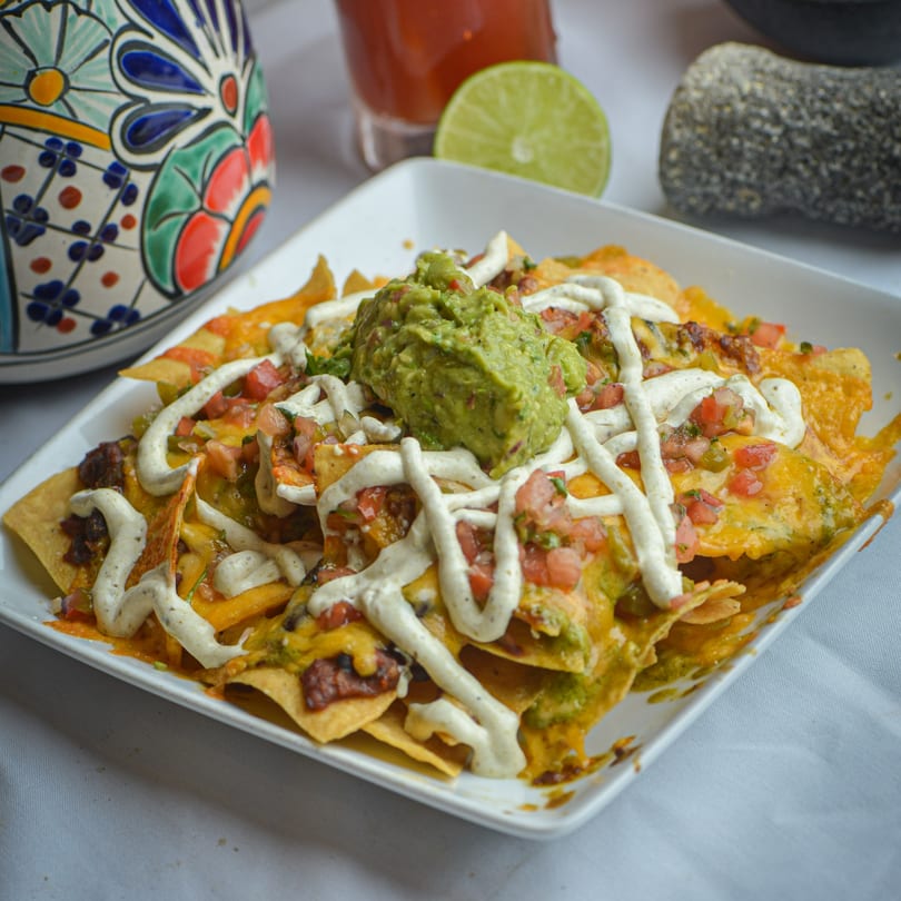 A plate of La Olla Mexican Cafe's nachos with guacamole, pico de gallo, and crema.