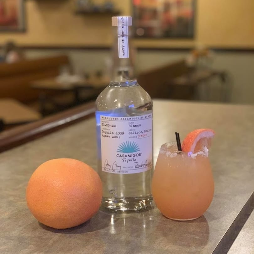 A bottle of Casamigos Tequila, a grapefruit, and a grapefruit margarita on a counter.
