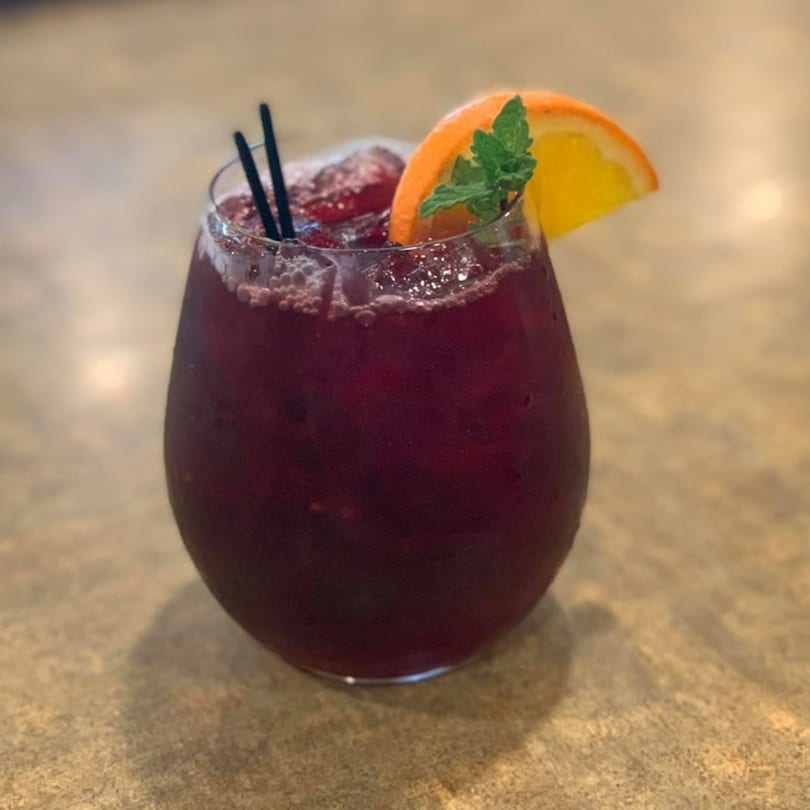 A La Olla Mexican Cafe sangria with orange slice, mint, and two black straws.