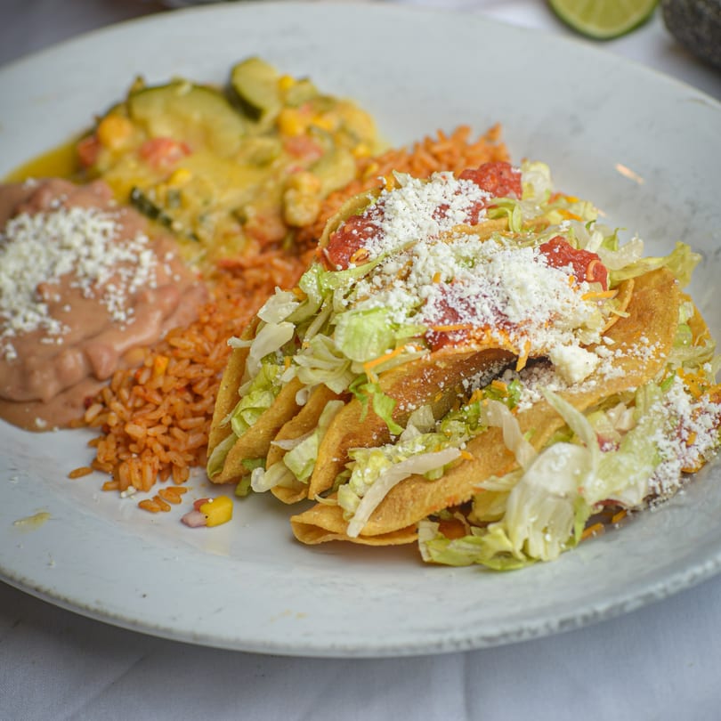 A plate of La Olla Mexican Cafe's tacos, rice, refried beans, and zucchini in cheese sauce.