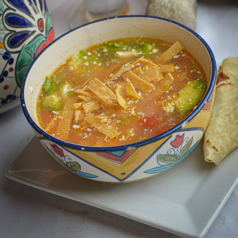 A colorful bowl of La Olla Mexican Cafe's tortilla soup with avocado, cheese, and tortilla strips.