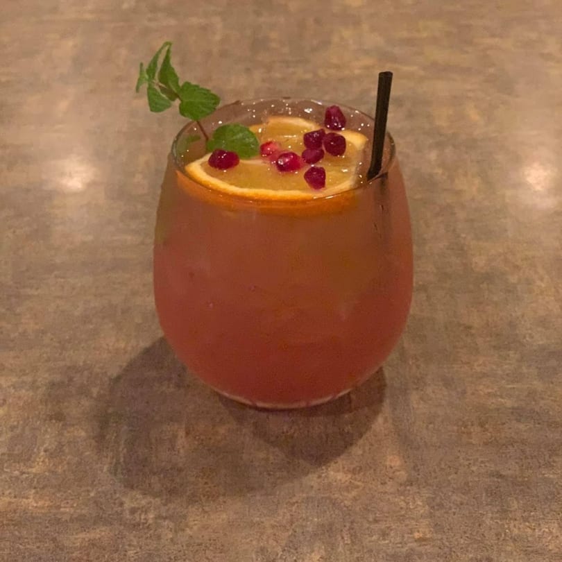 A La Olla Mexican Cafe cocktail with orange slices, pomegranate seeds, and mint garnish.