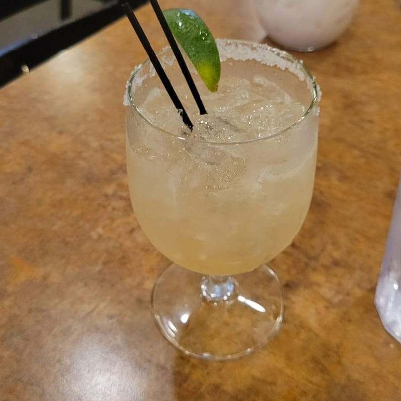 A La Olla Mexican Cafe margarita with a salted rim, lime wedge, and two black straws.