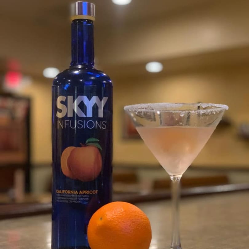 A bottle of Skyy Infusions California Apricot vodka, an orange, and a pink martini with a sugared rim.